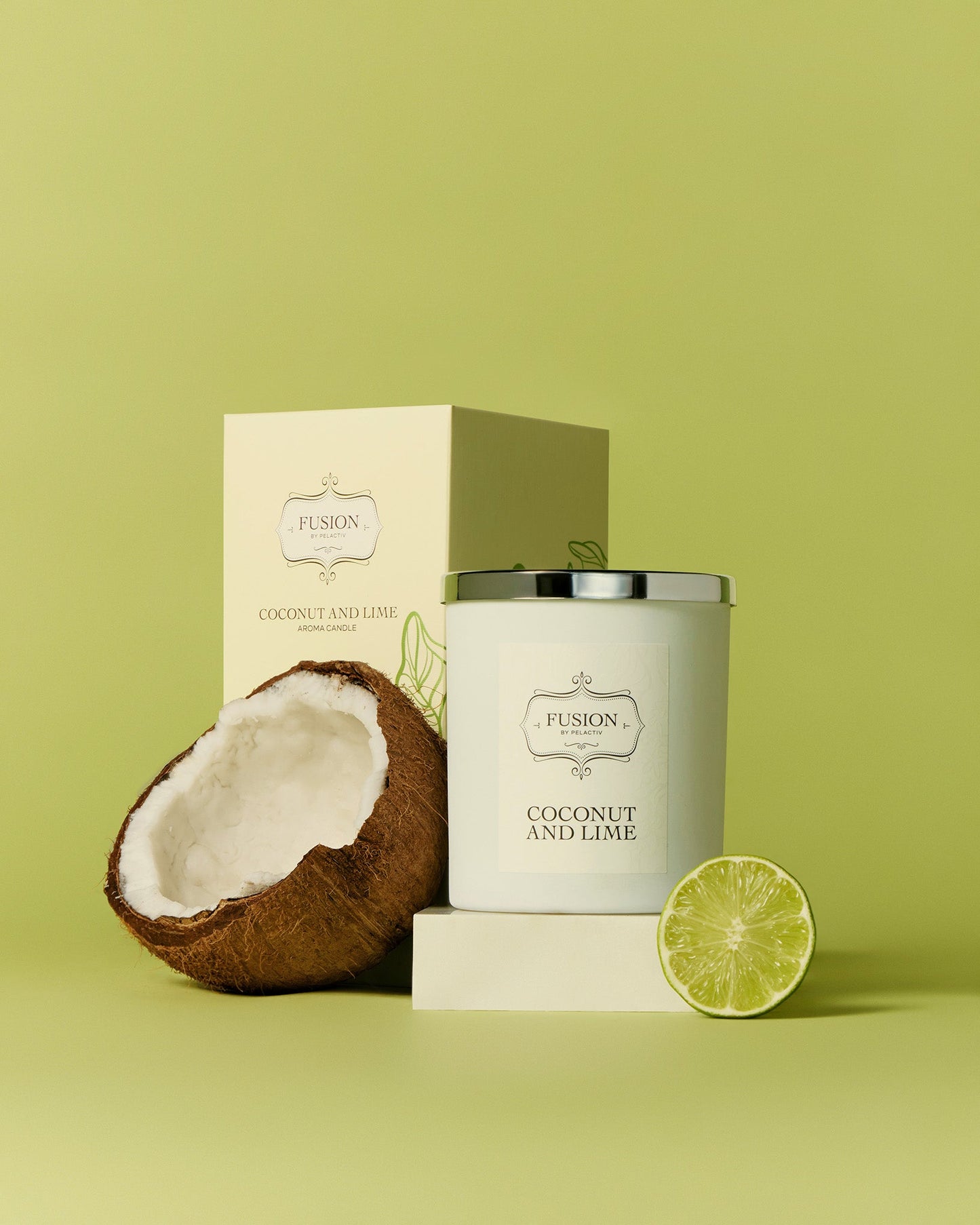 A coconut and lime candle with a silver lid is on a light green background, alongside half a coconut and a slice of lime, conveying a fresh, tropical vibe.