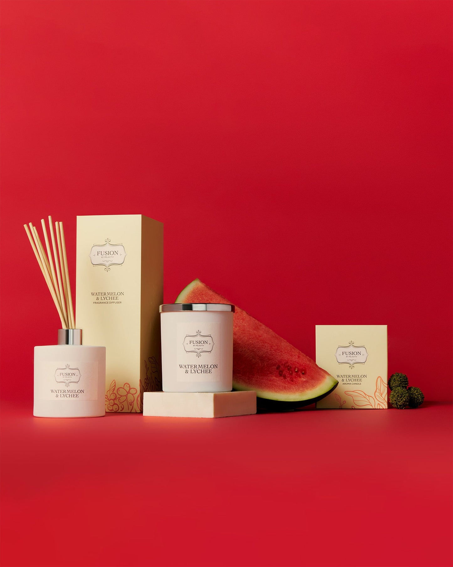A box of watermelon-scented candles next to a fresh watermelon and lychees, showcasing a vibrant and fruity theme.