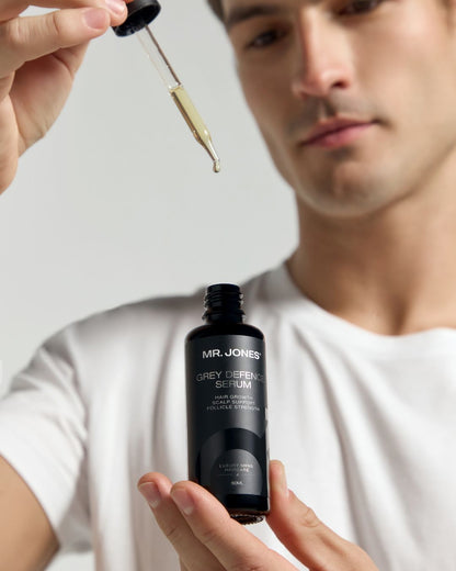 Person holding a bottle of 'MR. JONES GREY DEFENCE SERUM' with a dropper.