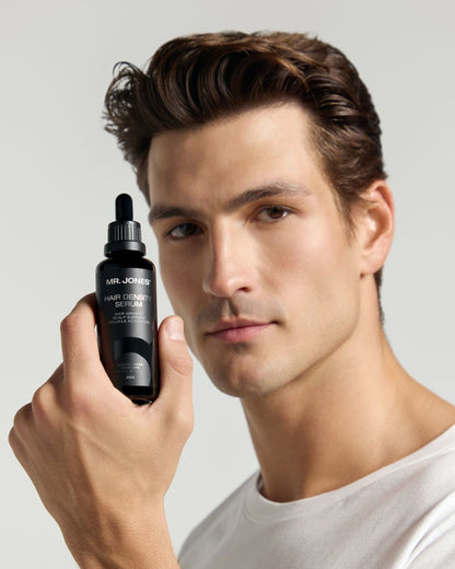 Man holding a bottle of Mr. Jones hair density serum against a neutral background