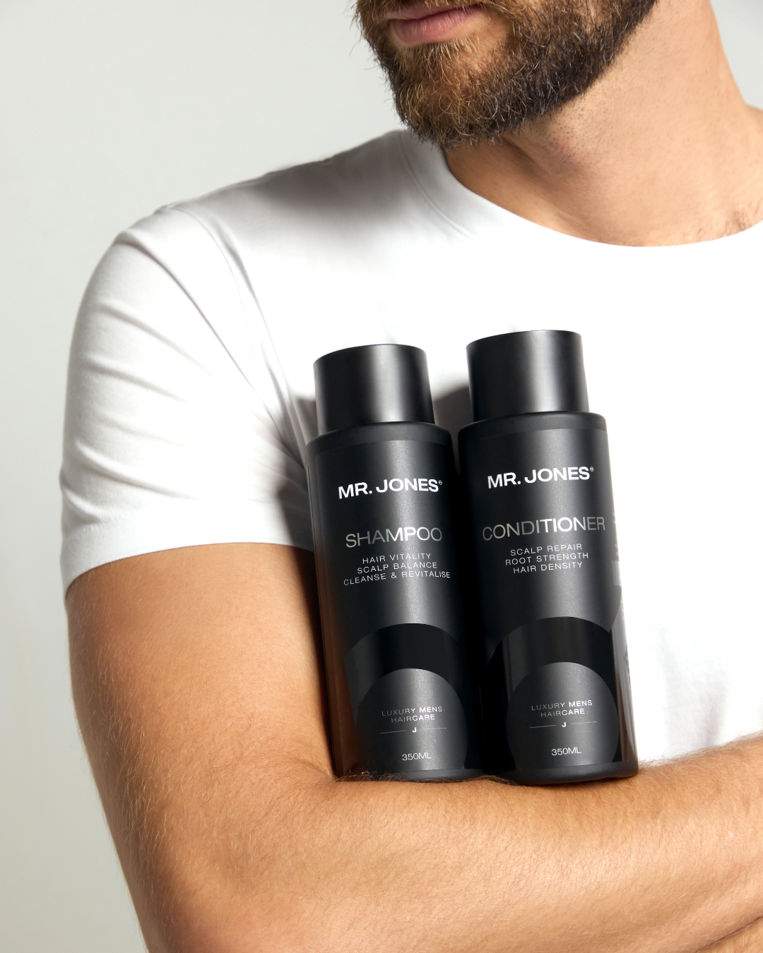 Two bottles of Mr. Jones shampoo and conditioner held by a person wearing a white t-shirt.
